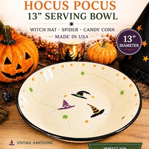 May include: A cream-colored ceramic serving bowl with a 13-inch diameter, featuring hand-painted illustrations of three witch hats, small green spiders, and candy corn motifs. The bowl has a black rim and is labeled Vintage Hartstone Hocus Pocus.