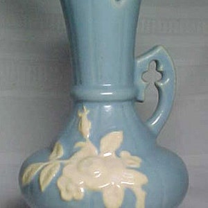 Puede incluir: Una jarra de cerámica azul con un diseño floral blanco. La jarra tiene un asa con un recorte decorativo y un pico ancho.