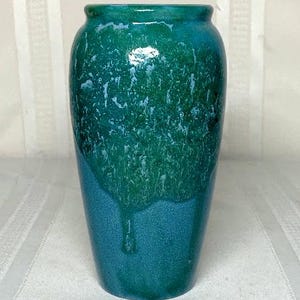 Könnte beinhalten: Eine glänzende Keramikvase mit einem Farbverlauf aus Türkis und Grün. Der obere Teil hat einen strukturierten, tropfenden Effekt, während der Boden einfarbig türkis ist. Die Vase hat einen abgerundeten Körper und einen leicht ausgestellten Rand. Sie ist etwa 20 cm hoch.