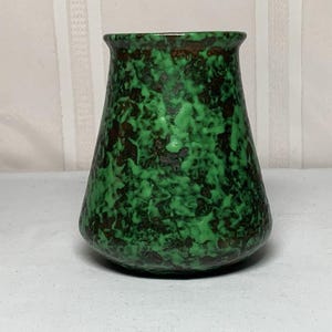 May include: A ceramic vase with a flared rim and a tapered body, featuring a mottled glaze pattern of vibrant green and dark brown colors. The surface has a textured appearance with an irregular, organic distribution of the two contrasting colors.