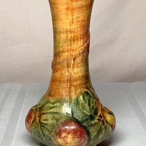 May include: A brown and green ceramic vase with a twisted design and a floral pattern. The vase has a wide base and a narrow neck.