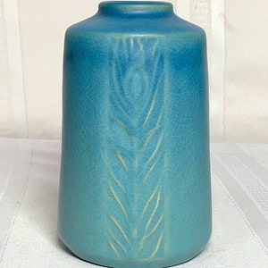 May include: A teal blue ceramic vase with a raised design of a stylized feather.