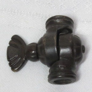 May include: A dark brown metal clamp with a decorative fin on one side. The clamp has a threaded end for attaching to a surface.