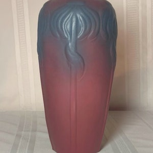 Puede incluir: Un jarrón alto de cerámica con un degradado de azul a rojo. El jarrón tiene un diseño floral estilizado en relieve en la superficie.