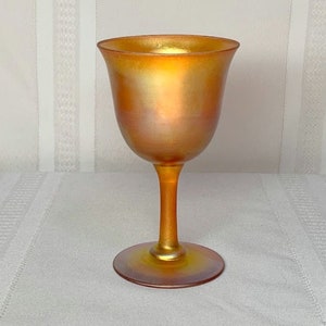 May include: A gold iridescent glass wine goblet with a flared bowl and a tall stem.