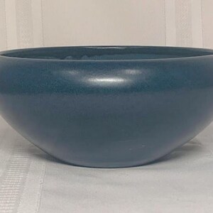 May include: A teal-colored ceramic bowl with a rounded shape. The bowl has a smooth, glossy finish and sits on a white surface. This decorative bowl is suitable for home decor.