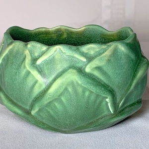 Puede incluir: Un macetero de cerámica verde con forma de col y superficie texturizada.