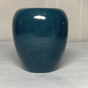 May include: A rounded, teal-colored ceramic vase with a smooth, glossy finish. The vase features a wide, bulbous body that tapers slightly toward the top opening, showcasing a deep, uniform blue-green hue with subtle light reflections on its surface.