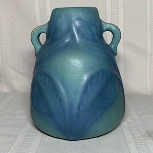 May include: A blue and teal ceramic vase with two handles. The vase has a rounded body and a flared opening. The color transitions from teal at the base to blue at the top, with a marbled effect.