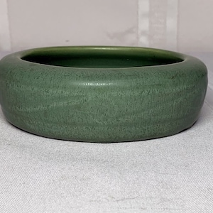 Puede incluir: Un cuenco de cerámica verde con una superficie texturizada. El cuenco es redondo y tiene un borde ligeramente acampanado.