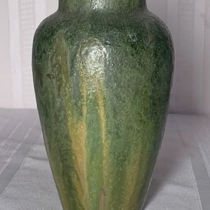 May include: A green ceramic vase with a textured surface and a mottled glaze. The vase has a rounded body and a narrow neck.