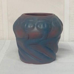 May include: A decorative vase with a unique, textured design. The vase features a blend of blue and red hues, with a swirling pattern on the exterior. The top opening is a darker shade of red. This piece is ideal for home decor.