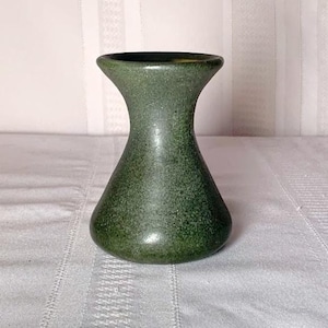 May include: A small, green speckled vase with a flared top and rounded base. The ceramic vase has a smooth, glossy finish and a classic, hourglass shape. The vase is suitable for displaying small flowers or as a decorative accent.