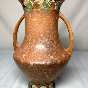 May include: A brown ceramic vase with a speckled glaze and two handles. The vase has a decorative rim with green and white floral designs.