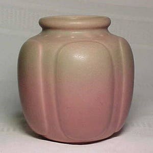 Puede incluir: Un pequeño jarrón de cerámica de color verde pálido y rosa con un cuerpo redondeado y crestas verticales. El jarrón tiene un acabado liso y brillante.