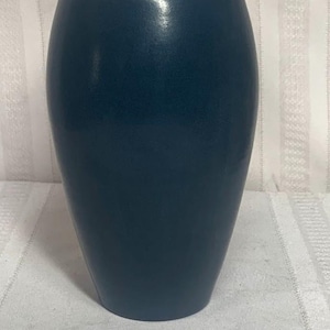 May include: A dark teal ceramic vase with a smooth, slightly textured surface. The vase has a rounded body and a tapered neck, suitable for displaying flowers or as a decorative accent piece. The vase is approximately 10 inches tall.