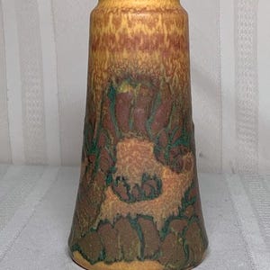 May include: A tall, decorative vase with a flared base and a narrow neck. The vase features a blend of colors, including yellow, brown, and green, with a textured, mottled appearance. The design has a floral pattern. The vase is approximately 10 inches tall.