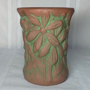 May include: A brown ceramic vase with a green glaze. The vase is decorated with a raised floral design.