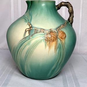 Puede incluir: Una jarra de cerámica esmaltada verde y crema con asa marrón y diseño de piña.