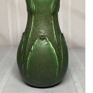 May include: A green ceramic vase with a textured surface and a bulbous shape. The vase features raised leaf-like designs and a narrow neck. The color is a deep, earthy green, suitable for home decor.