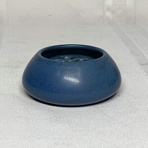 May include: A small, blue ceramic bowl with a rounded shape and a slightly indented center. The bowl has a matte finish and a subtle texture.