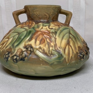 May include: A brown and green glazed ceramic vase with two handles and a floral design. The vase has a rounded body and a wide mouth.