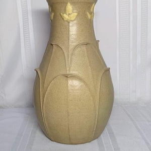 May include: A beige ceramic vase with a speckled finish. The vase has a bulbous body and a flared neck. The design includes stylized leaf accents in a lighter yellow color. The vase is approximately 10 inches tall.