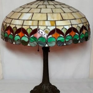 May include: A stained glass table lamp with a multi-colored, geometric design. The lamp has a bronze base with a decorative, floral design.