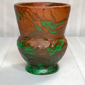 Puede incluir: Un jarrón de cerámica marrón con vetas verdes. El jarrón tiene una boca ancha y una base redondeada.
