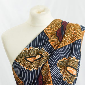 May include: A one-shoulder dress made from African wax print fabric. The fabric features a geometric pattern in shades of orange, blue, and red.