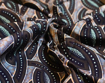 May include: Close-up of a folded fabric with a repeating pattern. The design features dark brown, white, and light blue curved shapes with dotted and striped details. The fabric has a textured appearance and a slight sheen.