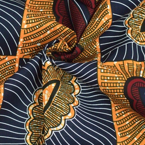 May include: A close-up of a fabric with a colorful African print pattern. The fabric is orange, blue, red, and white. The pattern features geometric shapes and lines.