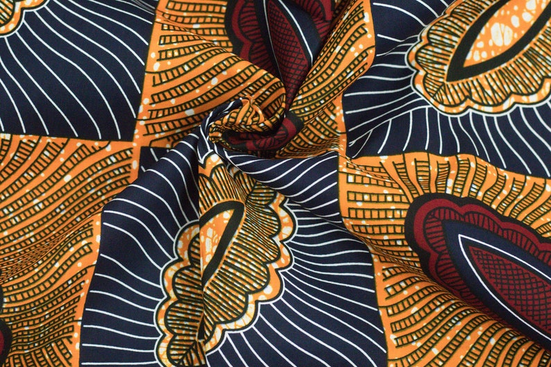 May include: A close-up of a fabric with a colorful African print pattern. The fabric is orange, blue, red, and white. The pattern features geometric shapes and lines.
