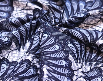 May include: Close-up of a folded fabric with a repeating pattern. The design features navy blue and white fan-like shapes with dotted details on a light gray background. The fabric appears to be cotton or a similar material, suitable for clothing or home decor.