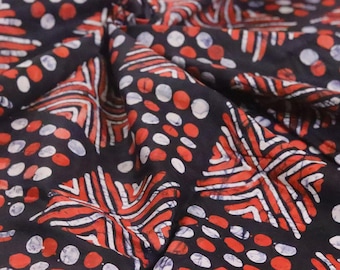Puede incluir: Primer plano de una tela oscura con un patrón repetitivo de formas geométricas rojas y blancas y lunares. La tela está doblada, creando sombras y profundidad. El diseño recuerda al batik o la impresión en bloque.