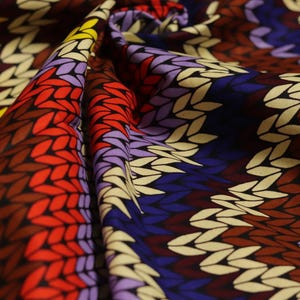 May include: A colorful fabric with a knitted pattern in shades of yellow, red, purple, brown, and blue.