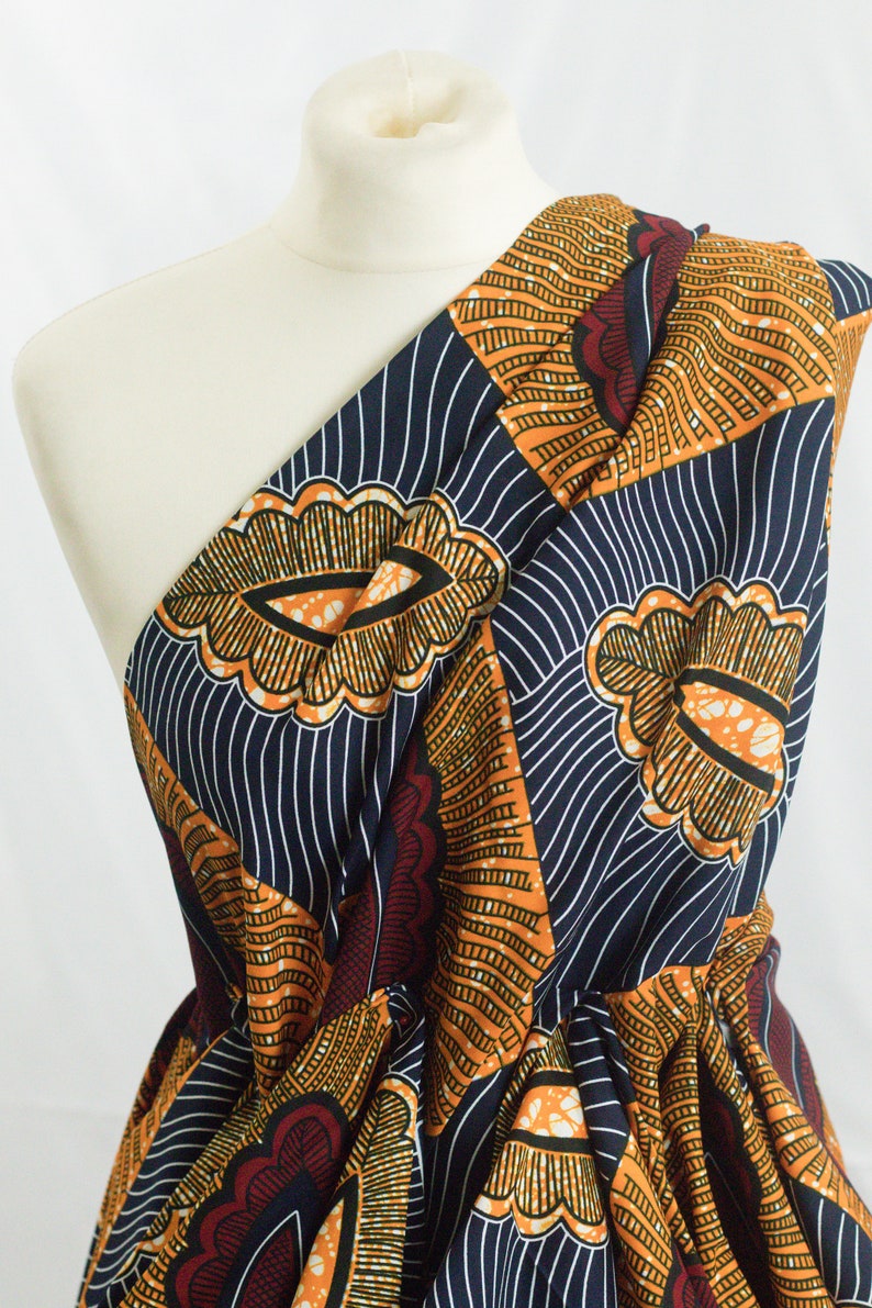 May include: A one-shoulder dress made from African wax print fabric. The fabric features a geometric pattern in shades of orange, blue, and red.