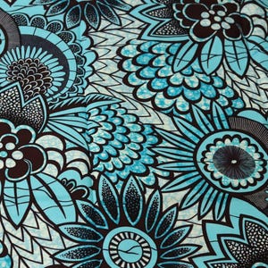 Op de afbeelding: Close-up van een stof met een herhalend bloemenpatroon. Het ontwerp toont grote gestileerde bloemen in tinten van teal, zwart en bruin tegen een witte achtergrond. De ingewikkelde details en het gedurfde kleurenpalet creëren een opvallend visueel effect.