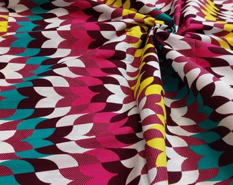 Op de afbeelding: Witte stof met een herhalend patroon van turquoise, roze en gele gebogen vormen. De stof is gevouwen en gedrapeerd.