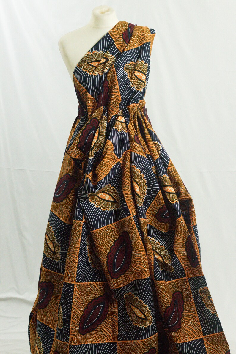 May include: A one-shoulder dress made from a colorful African print fabric. The fabric features a geometric pattern of orange, brown, and blue with a repeating design of stylized leaves.