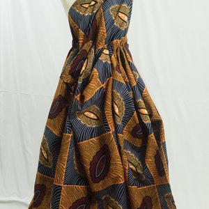May include: A one-shoulder dress made from a colorful African print fabric. The fabric features a geometric pattern of orange, brown, and blue with a white outline. The dress is gathered at the waist and has a flowing skirt.