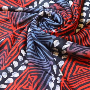 May include: Close-up of a fabric with a geometric pattern in shades of red, blue, and white. The fabric is folded and twisted, creating a dynamic and abstract design.