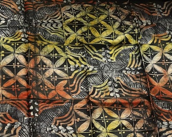 Puede incluir: Tela negra con un patrón batik en tonos naranja, amarillo y blanco. El patrón presenta flores y hojas estilizadas.