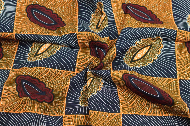 May include: A close-up of a fabric with a repeating pattern of orange, yellow, and blue geometric shapes. The fabric has a textured, woven look.