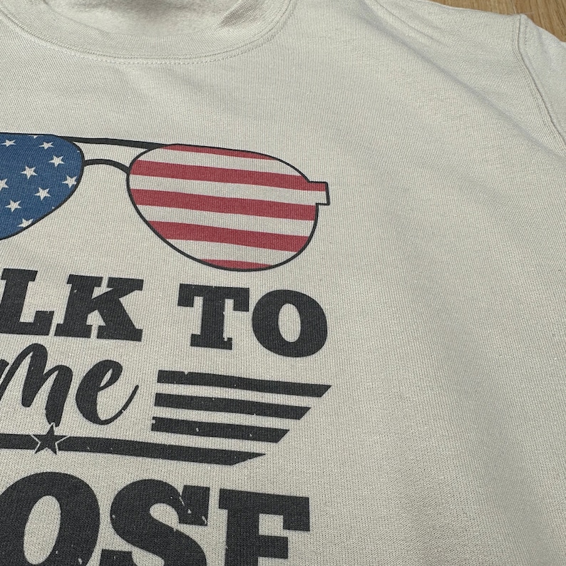 May include: A light gray sweatshirt with a graphic of sunglasses with an American flag design. The text "Talk to me close" is printed below the sunglasses.