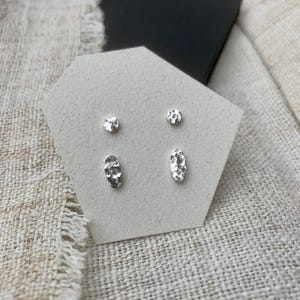 May include: A set of four silver earrings with textured surfaces. Two earrings are round and two are oval.