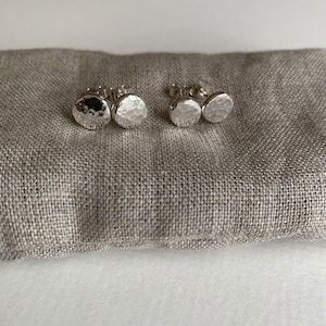 May include: A pair of silver hammered disc stud earrings. The earrings are round and have a textured surface.
