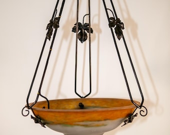 May include: A hanging bowl light fixture featuring a frosted glass basin with a gradient of amber orange at the top and a muted grey at the bottom. The bowl is suspended by three dark metal rods adorned with decorative metal leaf accents.