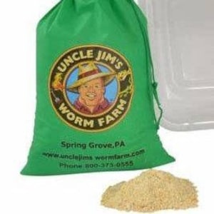 May include: A green drawstring bag with the text "UNCLE JIM'S WORM FARM" and an image of a man in a hat. The bag also includes the city and state, website, and phone number. A pile of light brown material sits in front of the bag.