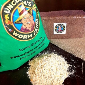 May include: A green bag with a cartoon man wearing a hat and the text "Uncle Jim's Worm Farm" on it. The bag is next to a brown brick of worm castings and a pile of shredded coconut coir. The text on the bag also includes the website and phone number for the farm.